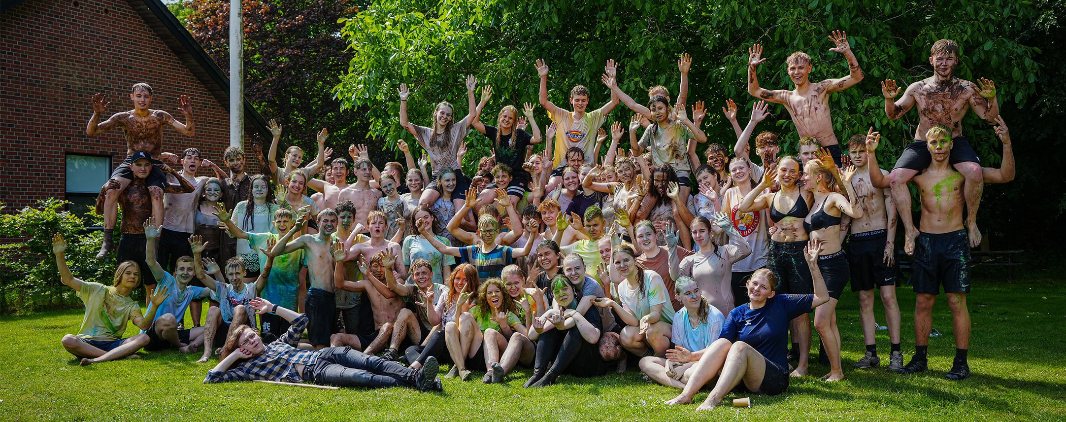 Farverige efterskoleelever nyder udendørsaktiviteter på Dronninglund Efterskole i Grønne omgivelser.